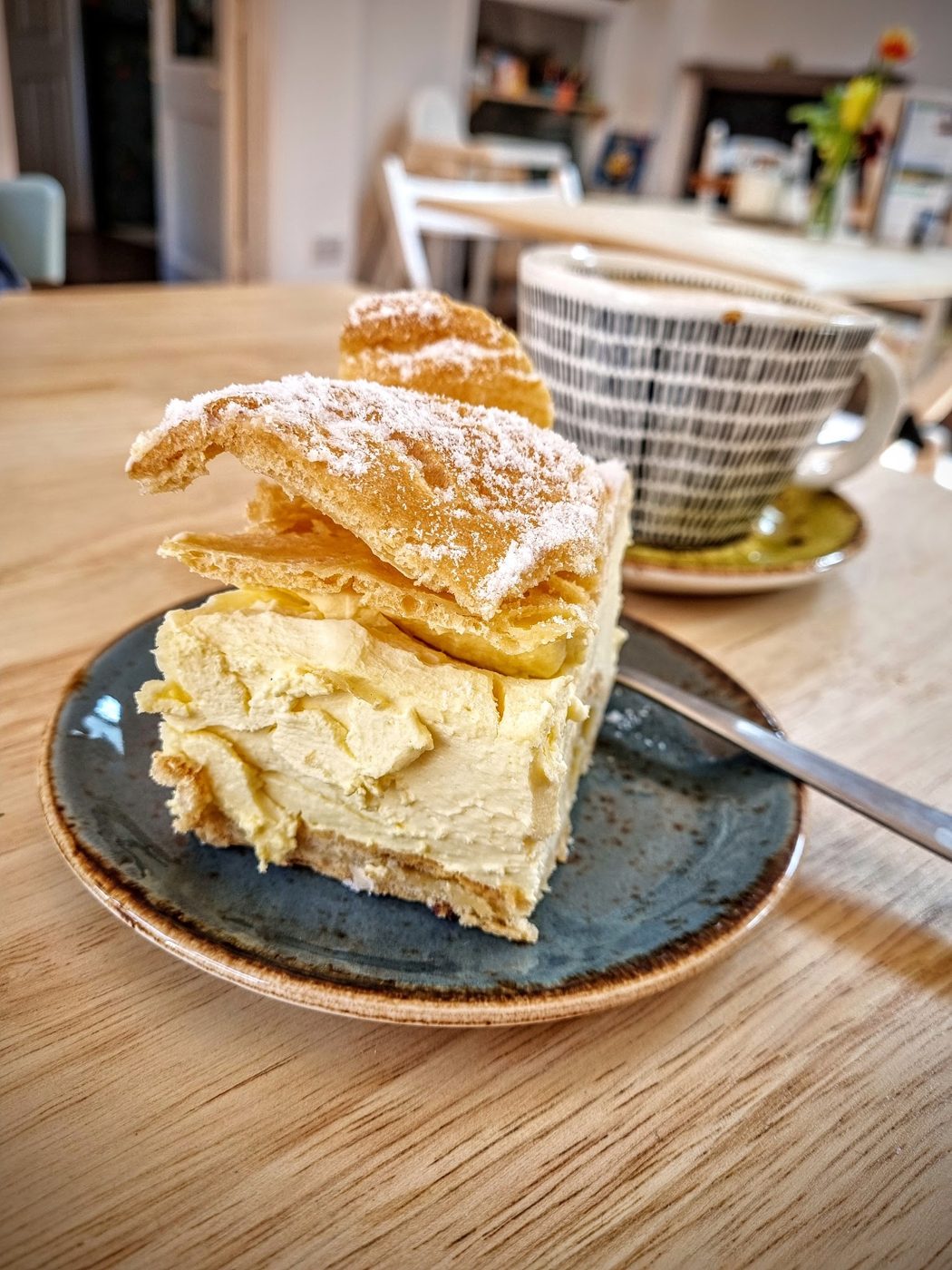 A slice of custard cream cake with a cup behind