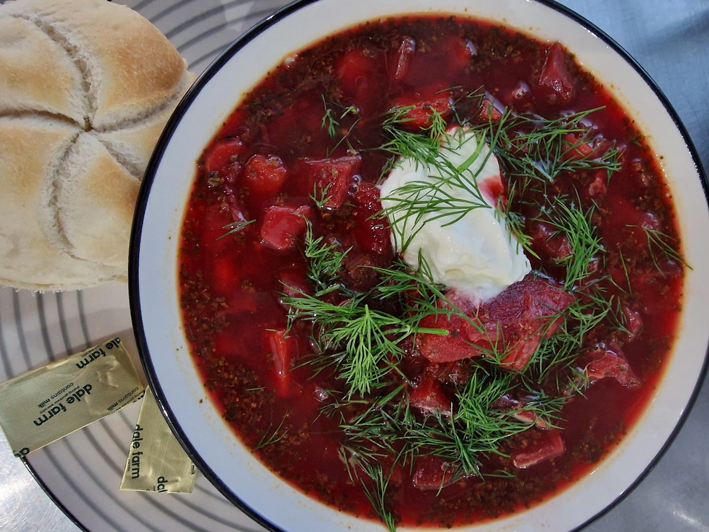 A bowl of red soup with dill and cream, with a bread roll