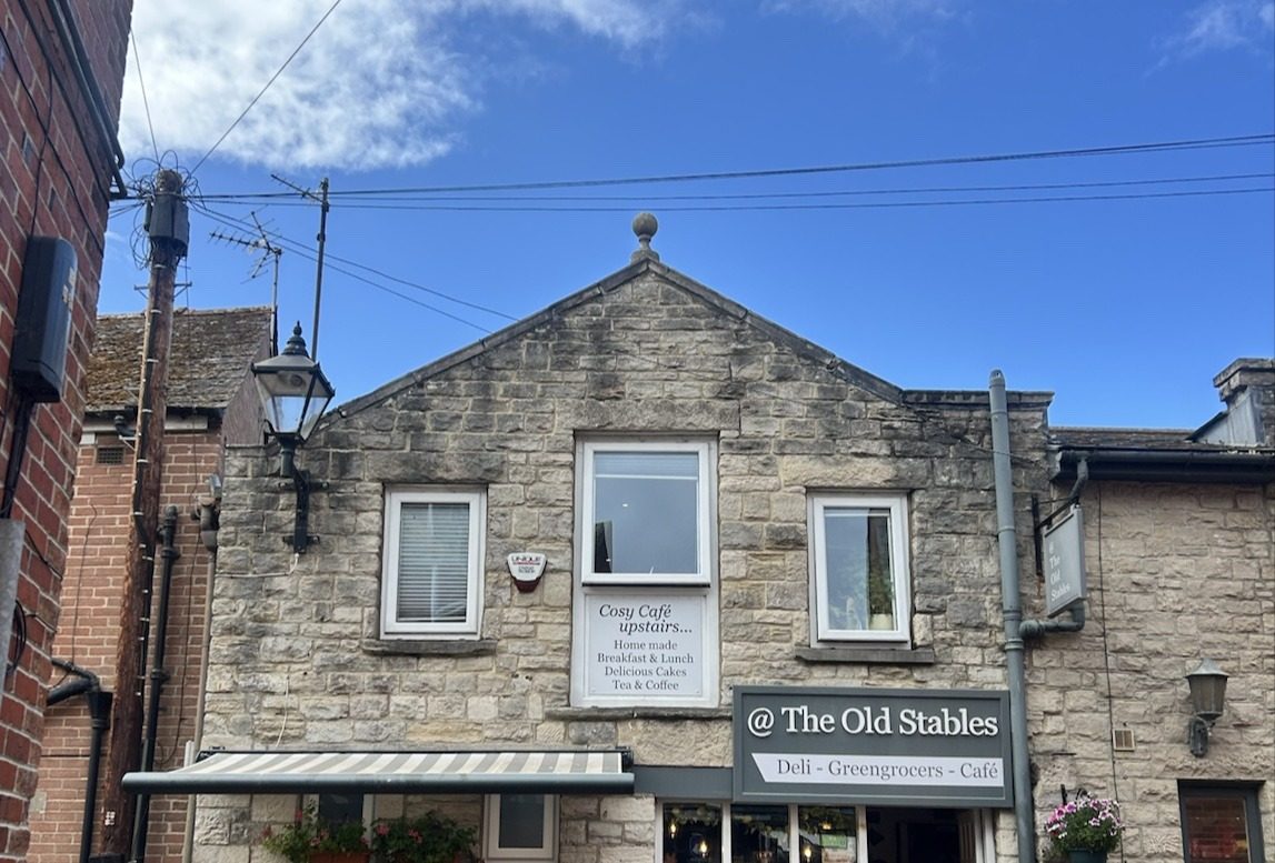 The stone gable with the @ The Old Stables Deli · Greengrocers · Café sign